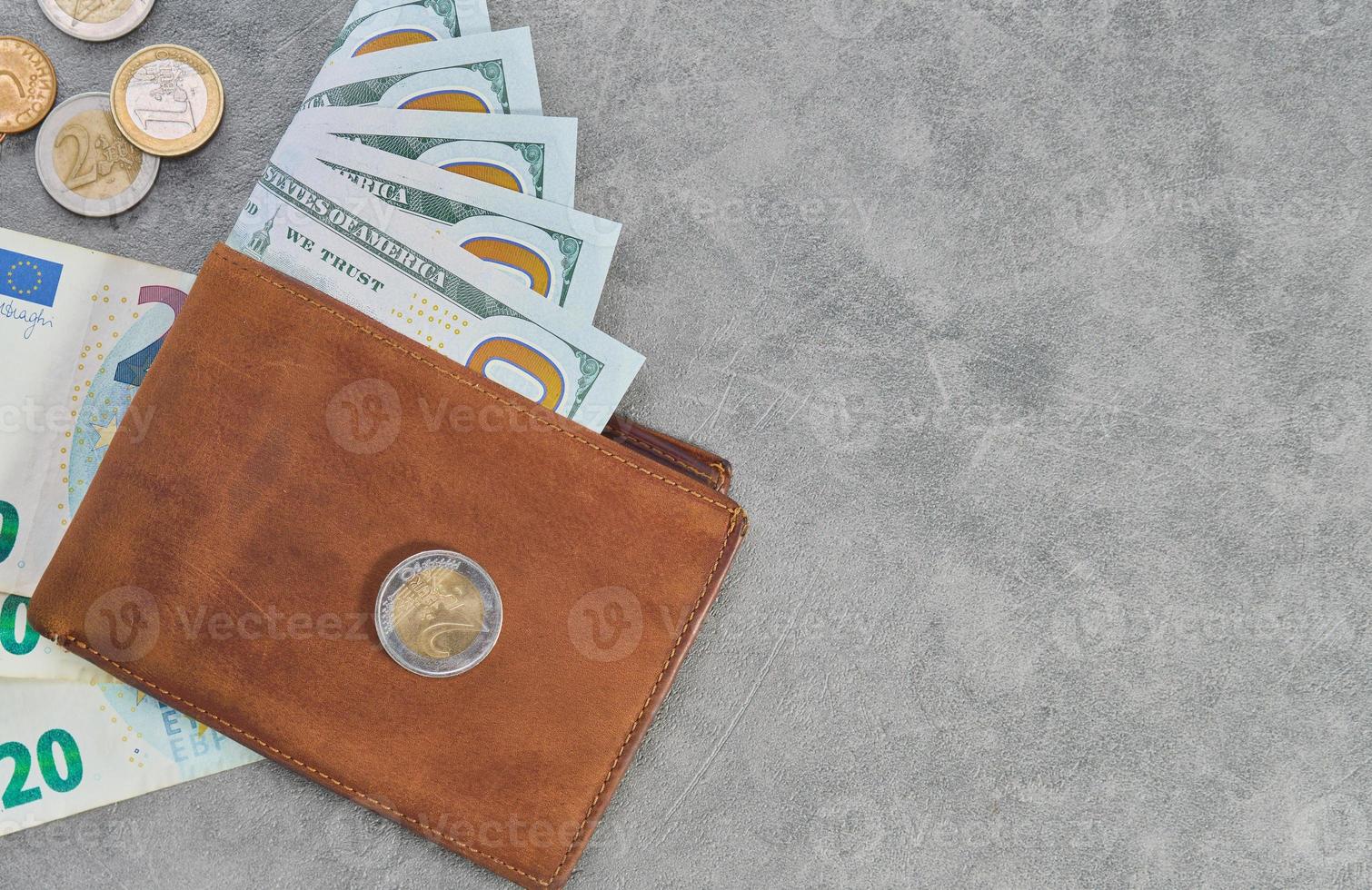 monedas en euros y billetes en dólares estadounidenses en cartera de cuero marrón sobre fondo de mesa gris, vista superior, concepto de financiación empresarial con espacio de copia foto