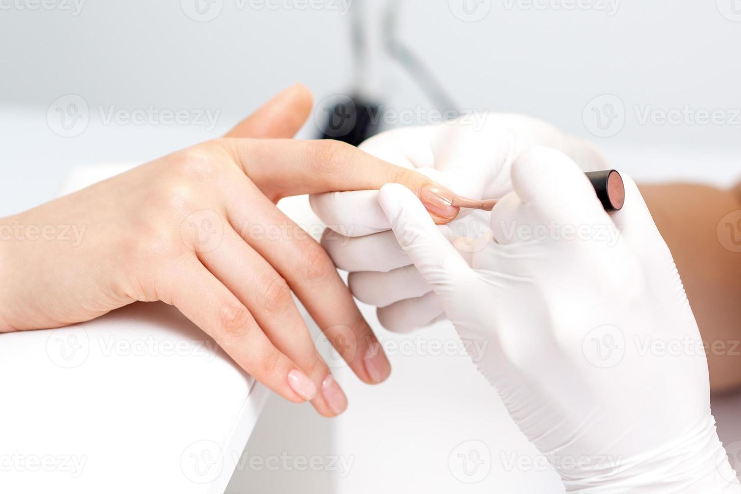 Manicure master applying beige nail polish photo