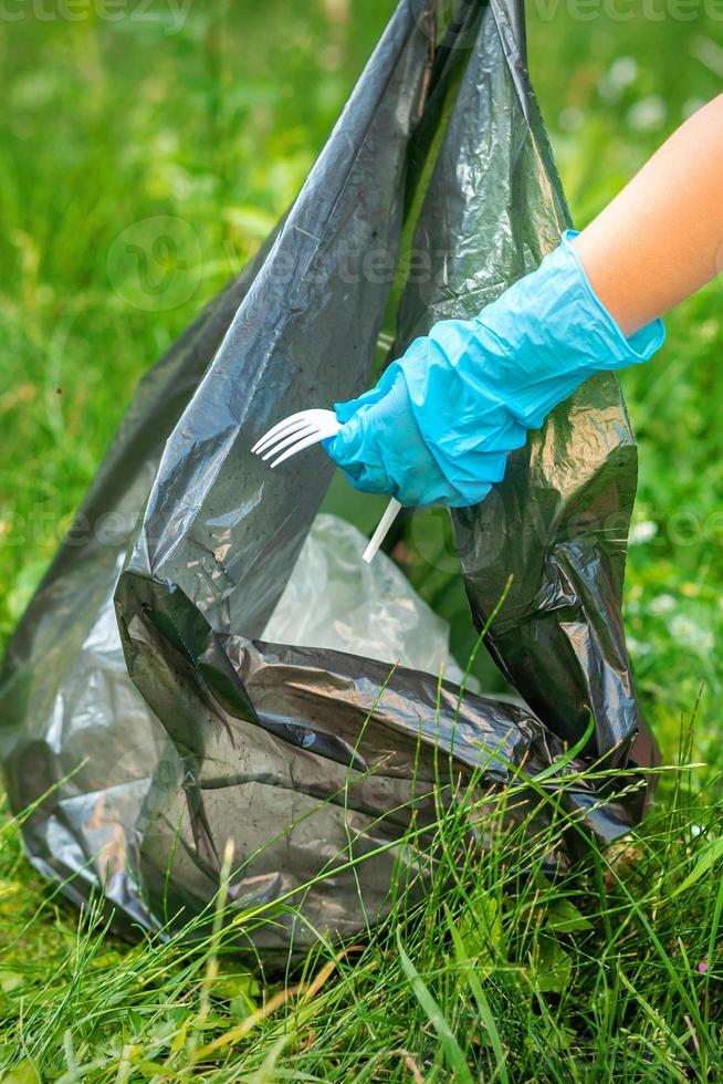 niño recoge basura plástica de la hierba foto