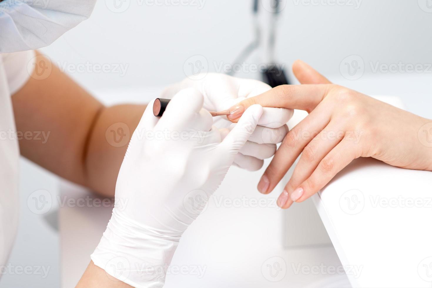 Manicure master applying beige nail polish photo