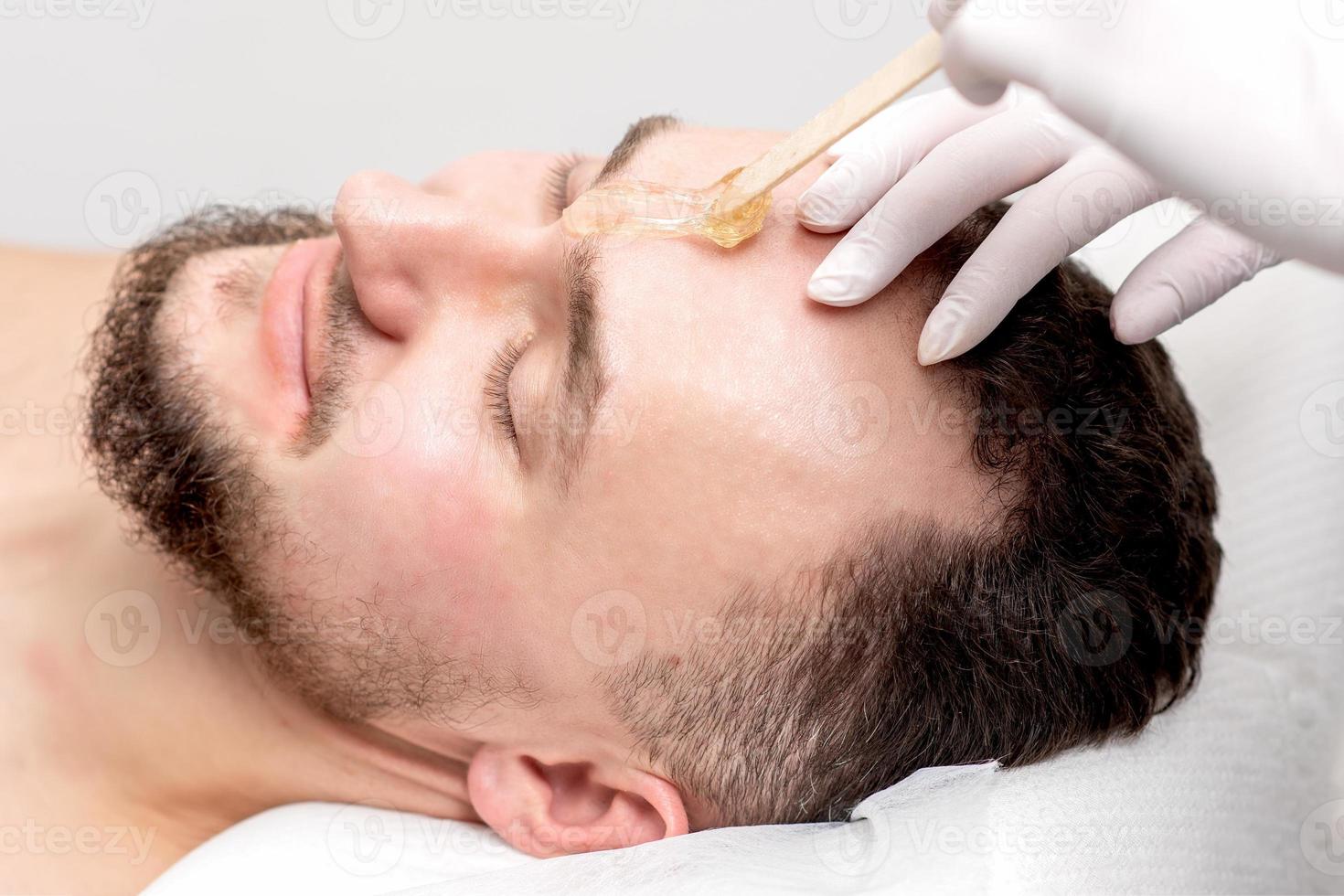 Beautician applies wax between male eyebrows photo