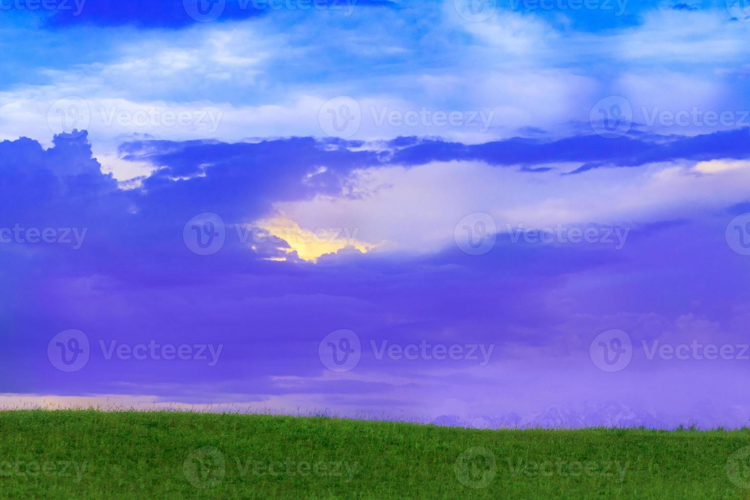 Landscape with sunset or dawn, hill with grass, mountains in the background, sun rays in the clouds. Copy space photo