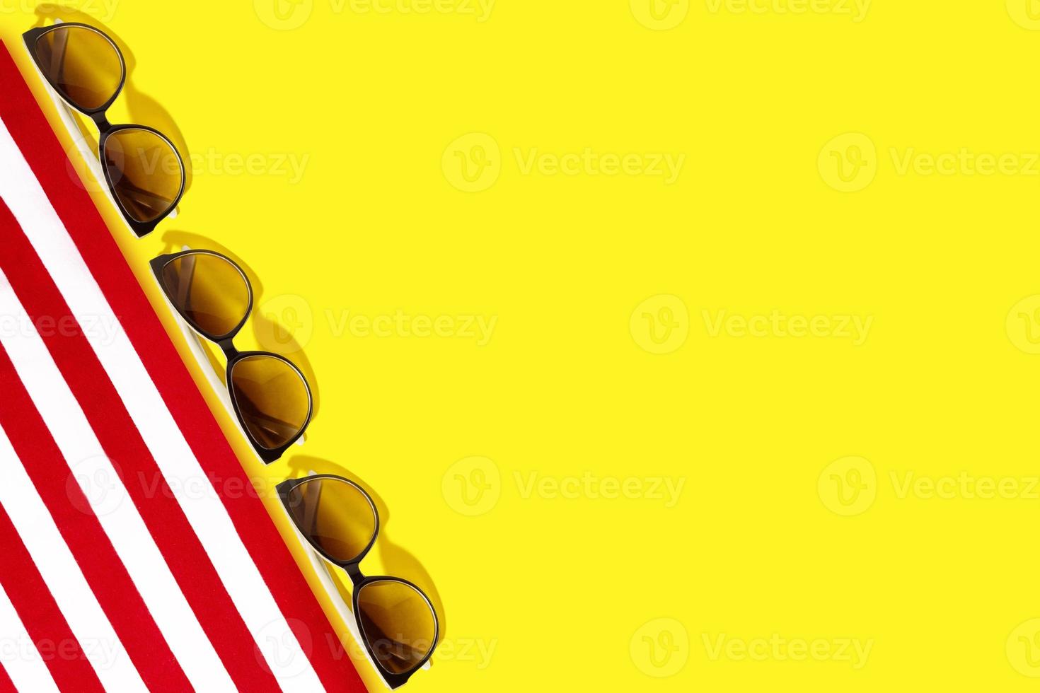 Red-white sunbed or towel, sunglasses, straw hat, seashells on a yellow background. Travel and tourism. Copy space photo