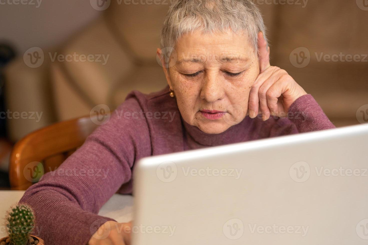 A senior woman sitting in front of a laptop communicates online through social networks. photo