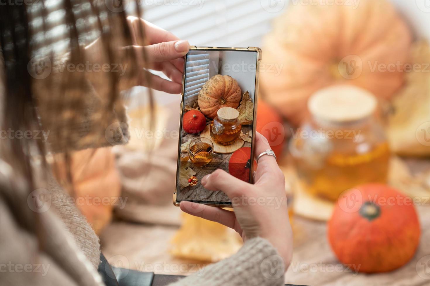 Girl taking photo of pumpkins, autumn leaves and teapot on a window. Girl photographing on phone rustic halloween composition. Happy Thanksgiving and Halloween