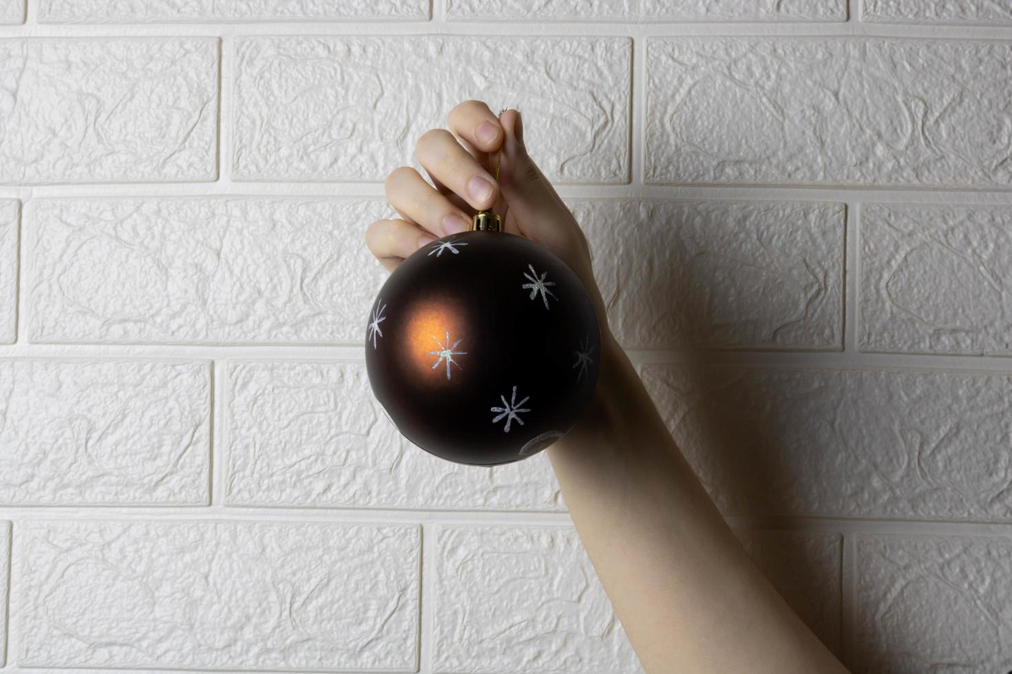 A hand and a Christmas tree ball highlighted on a white brick wall background. photo