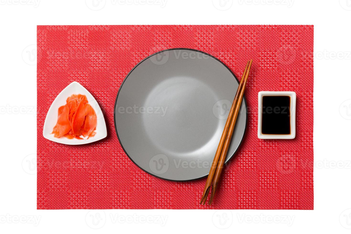 Empty round gray plate with chopsticks for sushi and soy sauce, ginger on red mat sushi background. Top view with copy space for you design photo