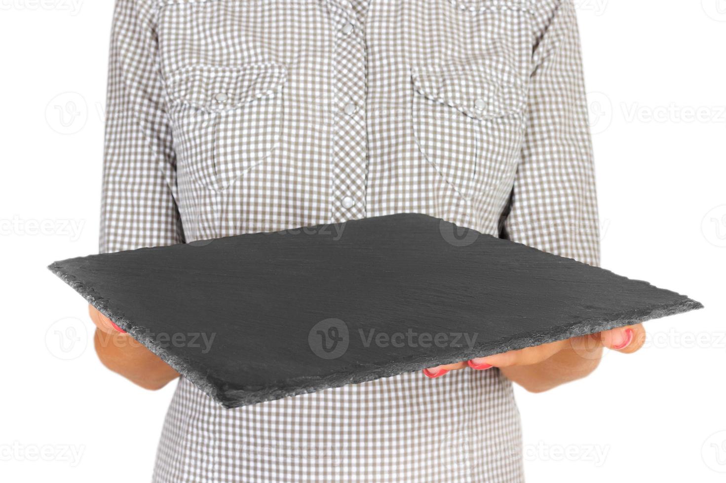 girl in the plaid shirt is holding an empty black square slate plate in front of her. woman hand hold empty dish for you desing. perspective view, isolated on white background photo