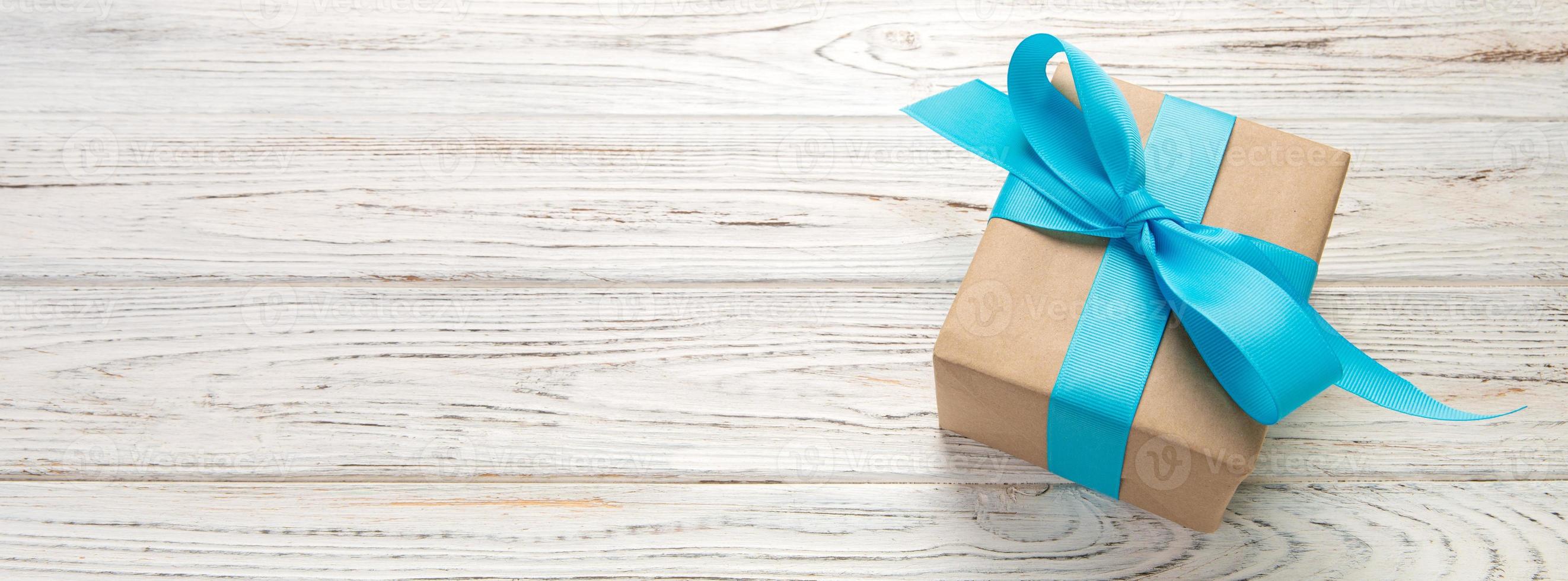 Beautiful gift box with a blue bow on the white wooden table. Top view banner with copy space for you design photo