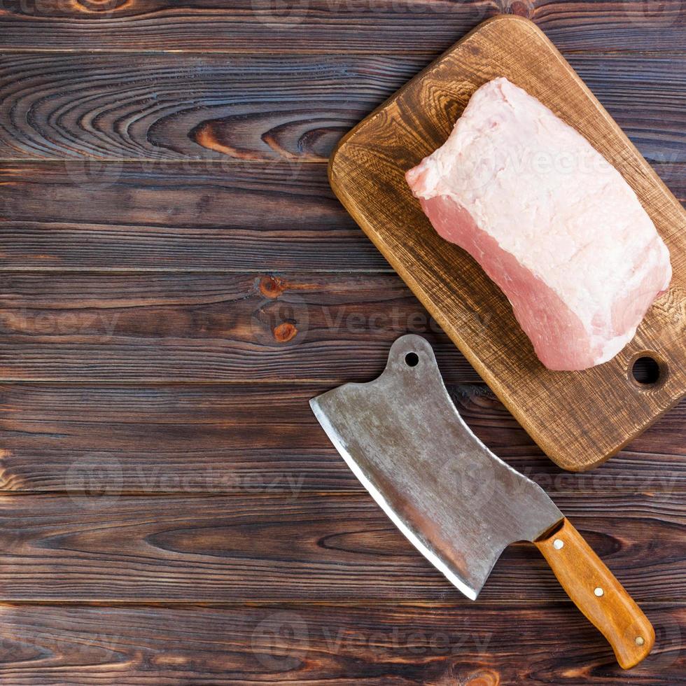 Raw cut of pork shoulder on board with knife or Kitchen ax. cleaver with fresh raw meat on black wooden background photo
