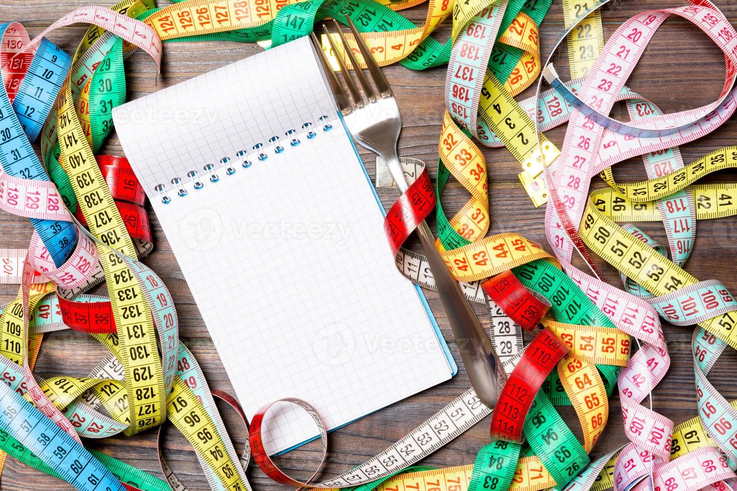 Group of colorful measure tapes, open notebook and fork on wooden background with empty space for your idea. Top view of healthy lifestyle concept photo