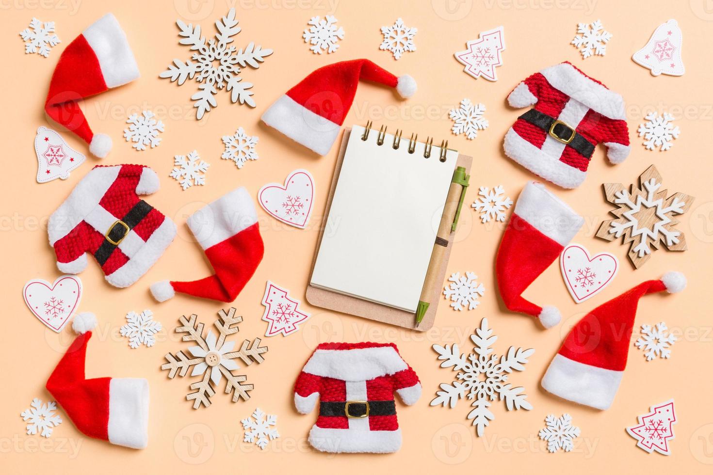 Top view of notebook with Christmas decorations and Santa hats on orange background. Happy holiday concept photo