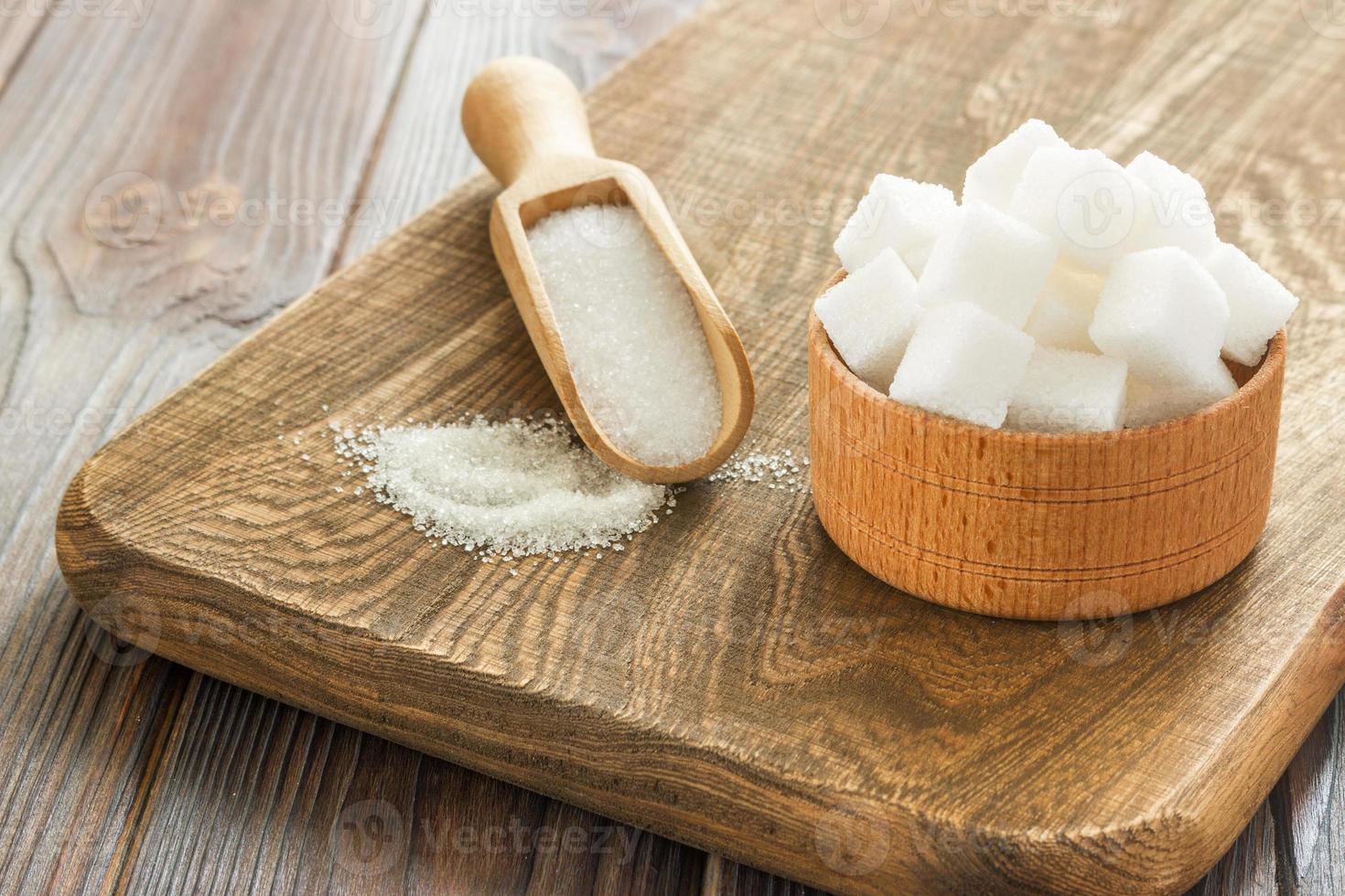 Bowl and scoop with white sand and lump sugar on wooden background photo