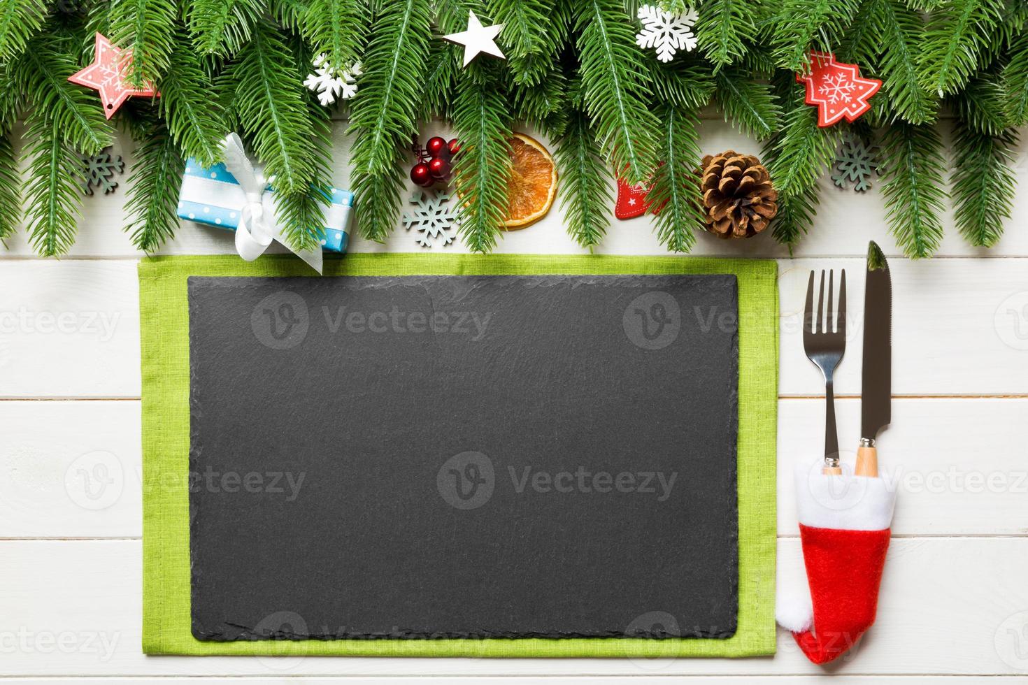 Top view of Christmas dinner on wooden background. Plate, utensil, fir tree and holiday decorations with copy space. New Year time concept photo