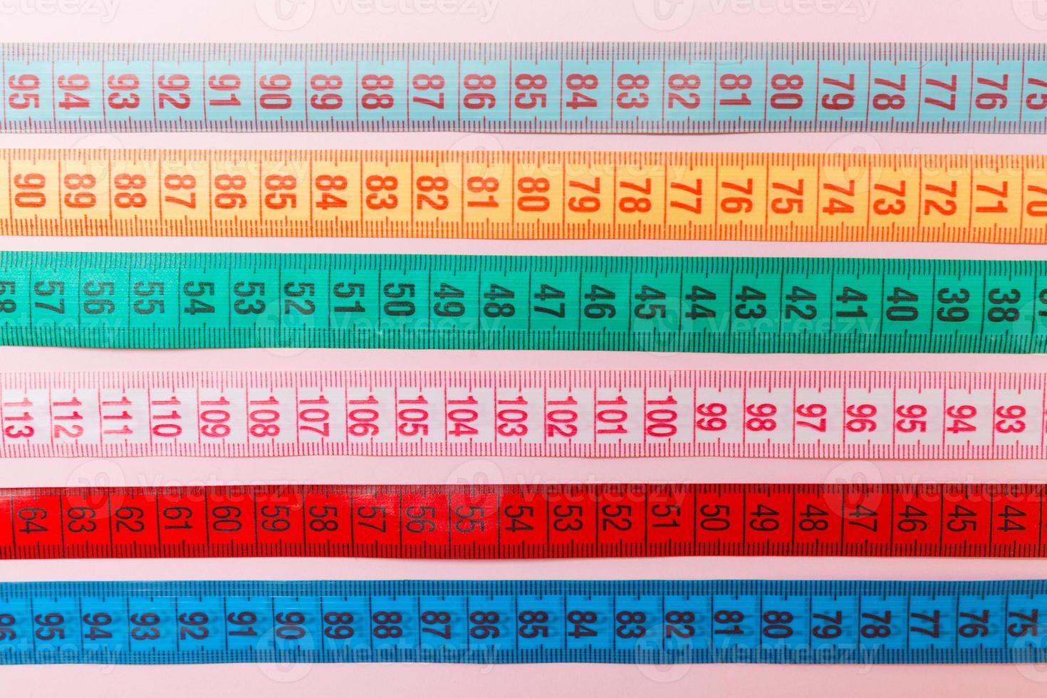 Close up of a group of colorful measure tapes lying in rows as a background. Diet concept on pink background photo