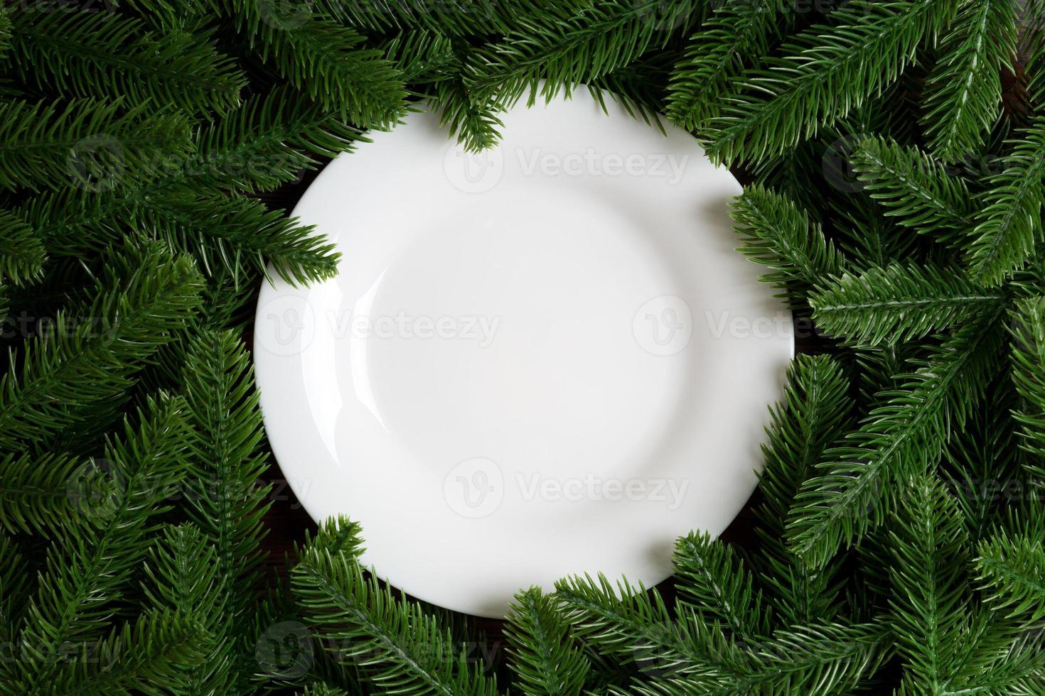 Top view of white plate surrounded with fir tree branches. Christmas dinner concept with copy space photo