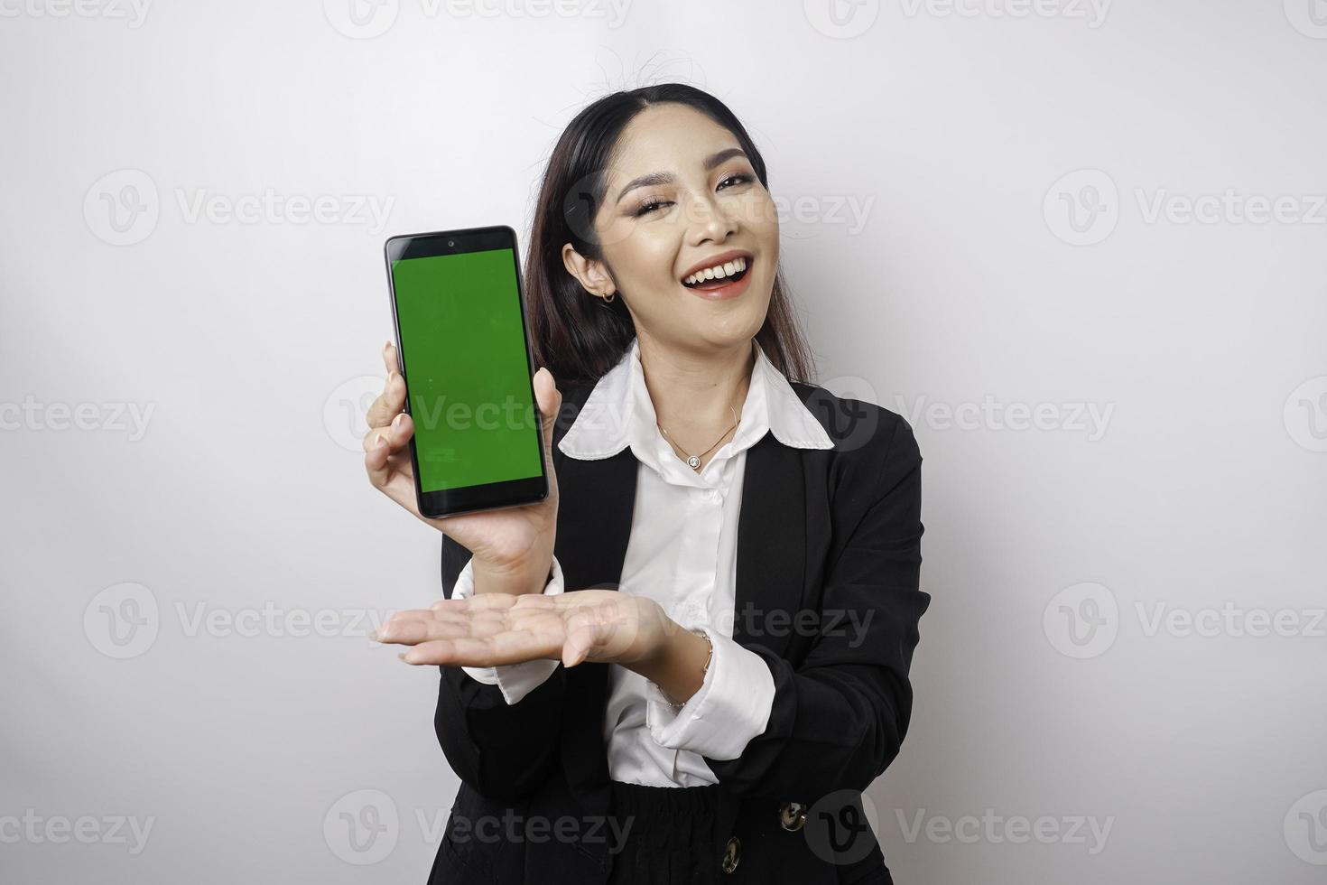 A happy young businesswoman is wearing black suit, showing copy space on her phone isolated by white background photo