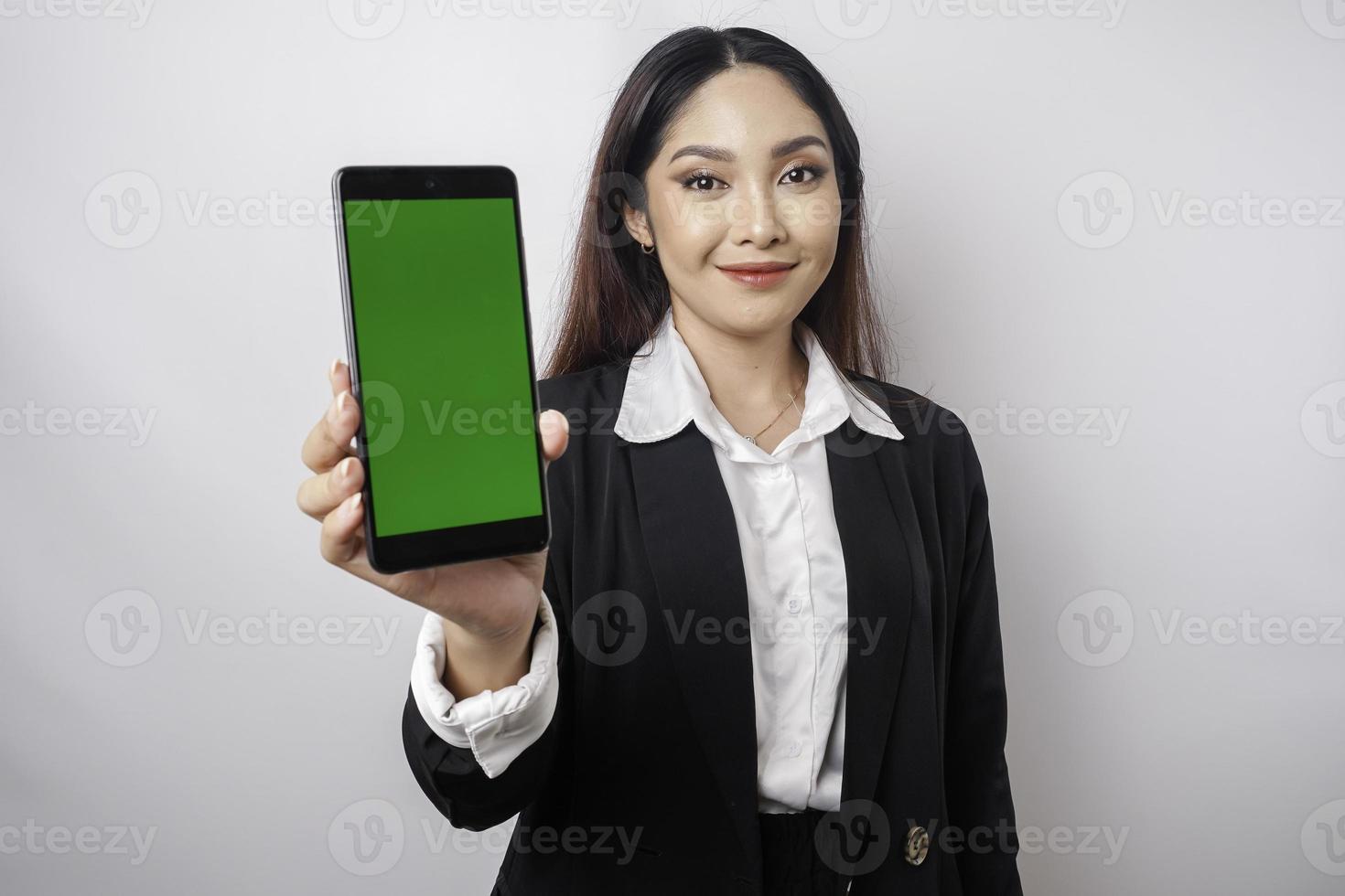 A happy young businesswoman is wearing black suit, showing copy space on her phone isolated by white background photo