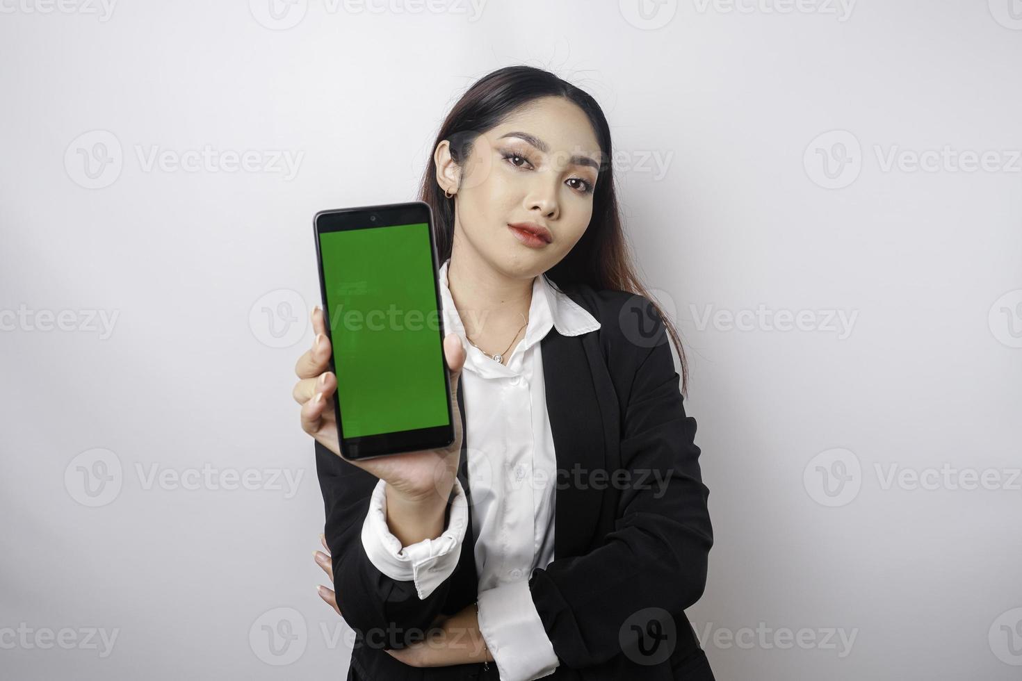 A happy young businesswoman is wearing black suit, showing copy space on her phone isolated by white background photo