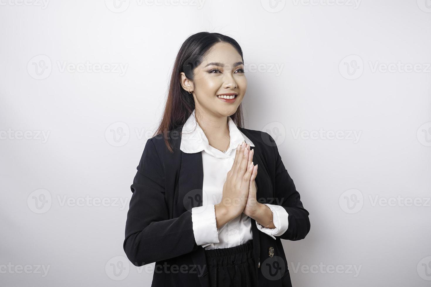 una joven empleada asiática sonriente que lleva un traje negro hace un gesto con un saludo tradicional aislado sobre fondo blanco foto