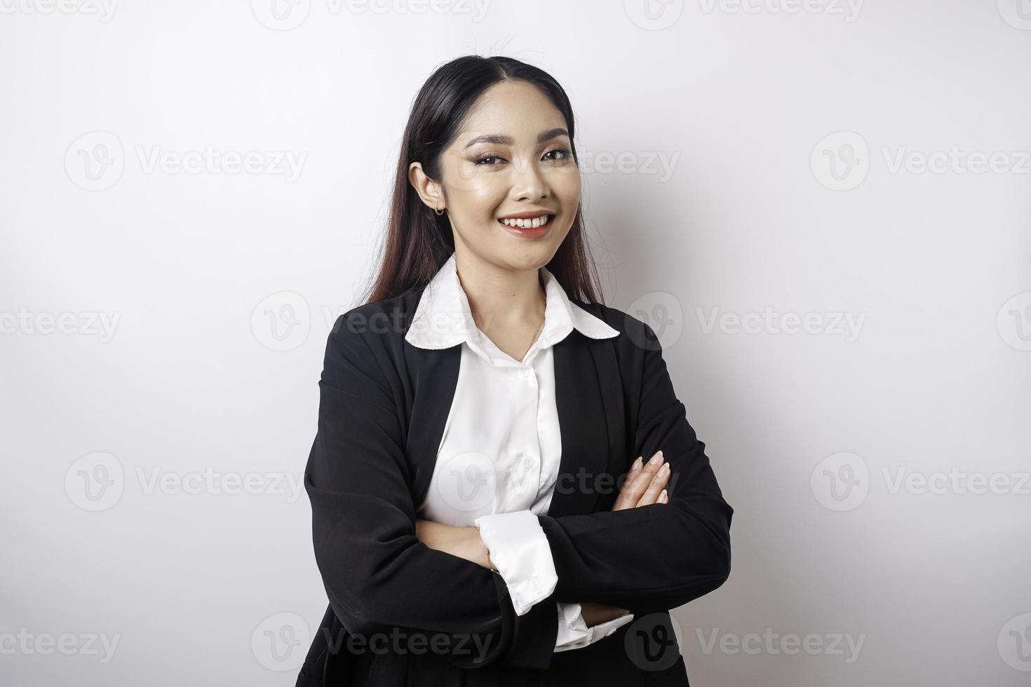 retrato de una jefa asiática sonriente y confiada con traje negro parada con los brazos cruzados y mirando la cámara aislada sobre fondo blanco foto