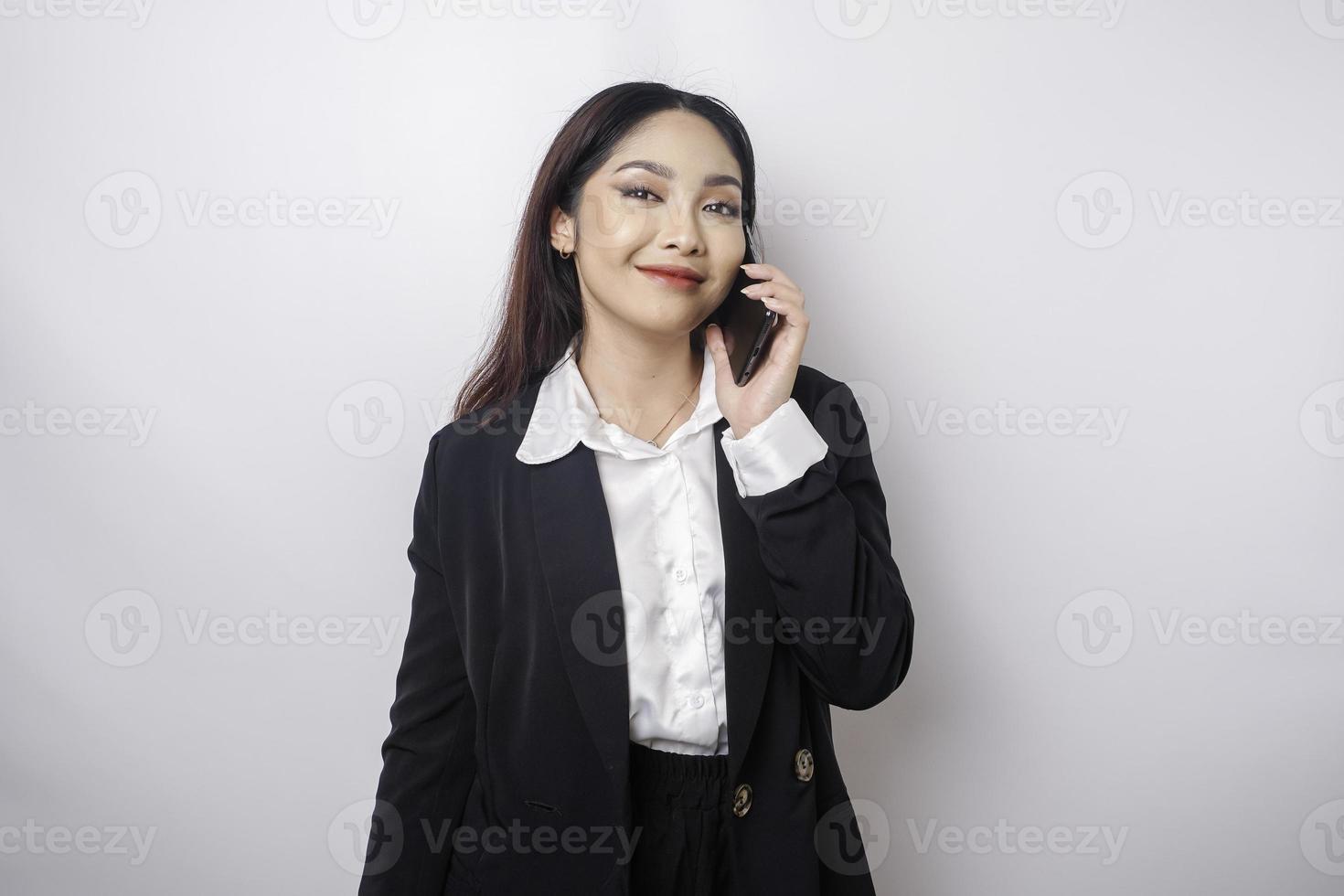 A portrait of a happy Asian businesswoman is smiling while talking on phone call wearing a black suit isolated by a white background photo