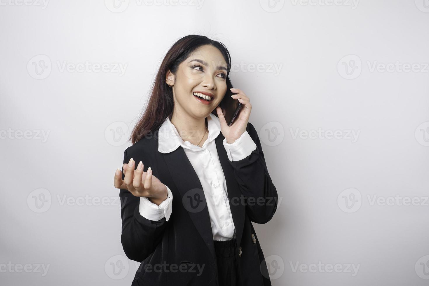 A portrait of a happy Asian businesswoman is smiling while talking on phone call wearing a black suit isolated by a white background photo