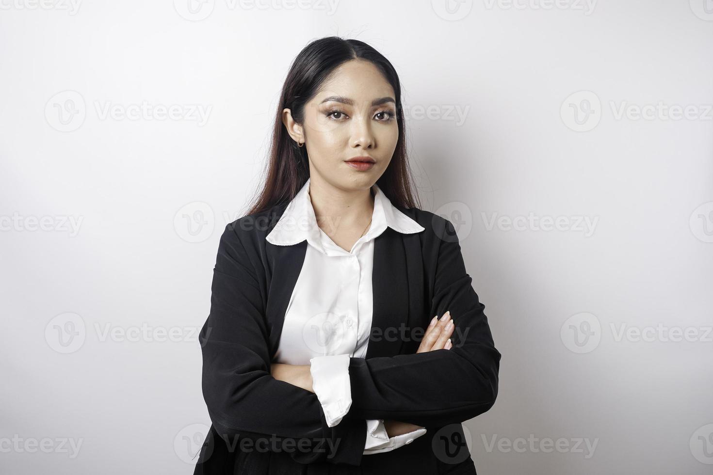 retrato de una jefa asiática sonriente y confiada con traje negro parada con los brazos cruzados y mirando la cámara aislada sobre fondo blanco foto