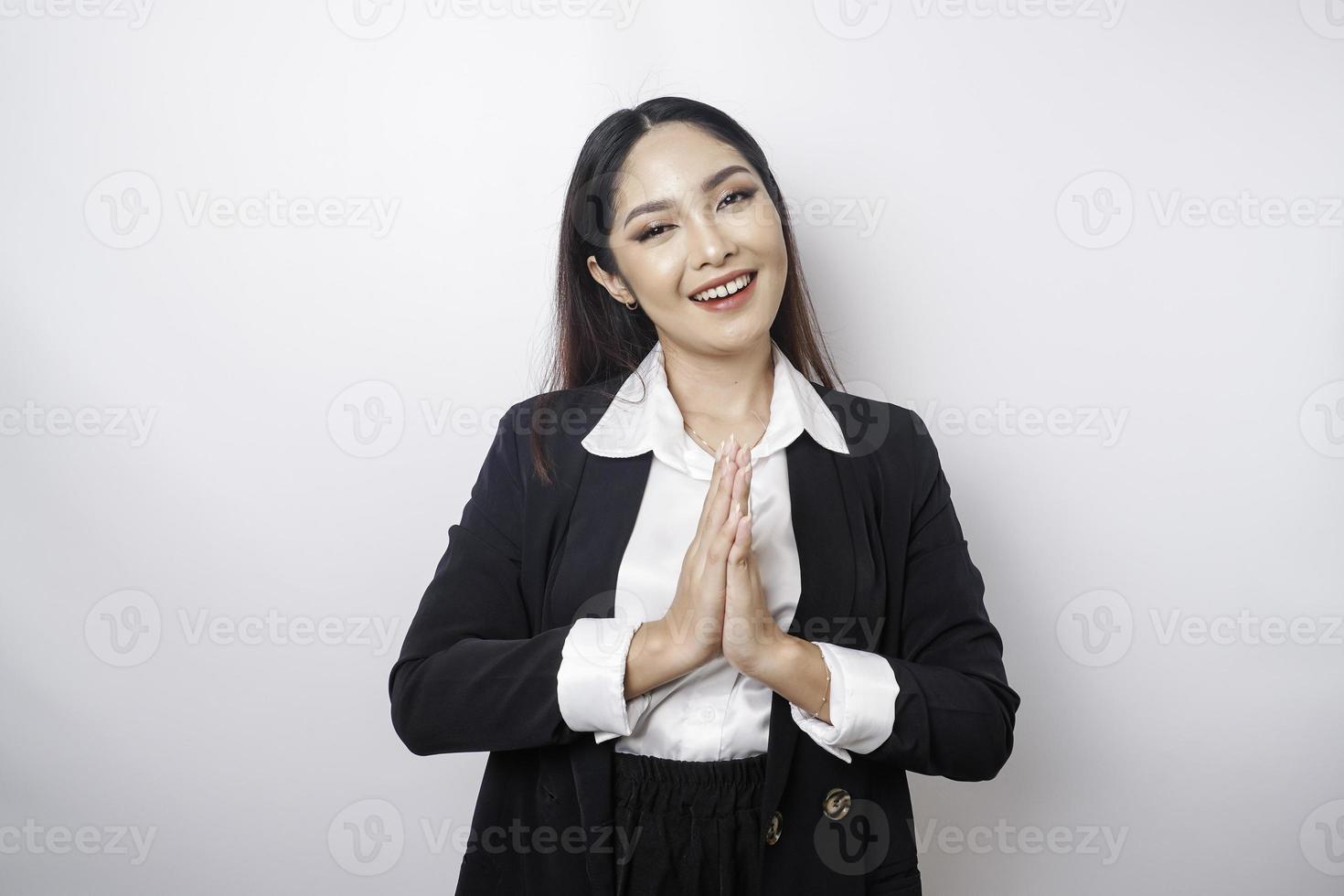 A smiling young Asian woman employee wearing a black suit gestures a traditional greeting isolated over white background photo