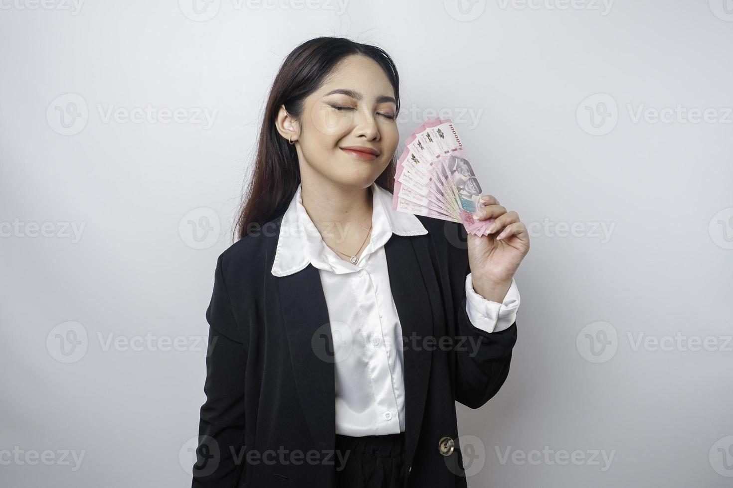 A happy young businesswoman is wearing black suit and holding cash money in Indonesian rupiah isolated by white background photo