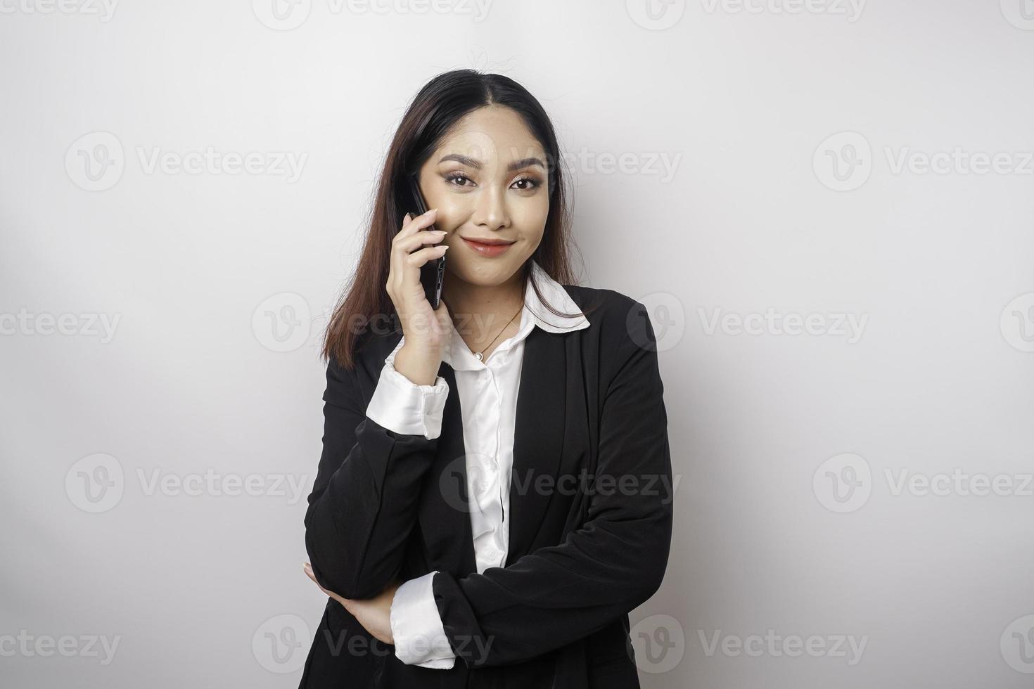 A portrait of a happy Asian businesswoman is smiling while talking on phone call wearing a black suit isolated by a white background photo