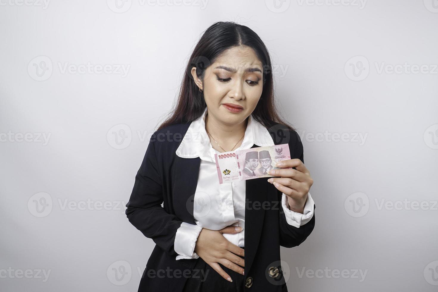 foto de una joven empresaria hambrienta y emocionada sosteniendo dinero en rupias indonesias y preguntándose qué pedir comida deliciosa aislada en un fondo de color blanco