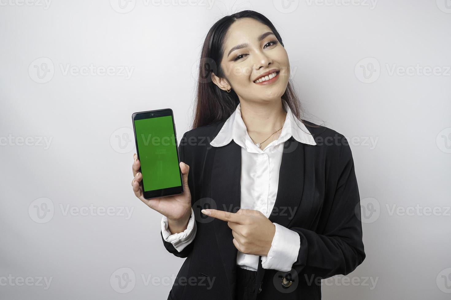 A happy young businesswoman is wearing black suit, showing copy space on her phone isolated by white background photo