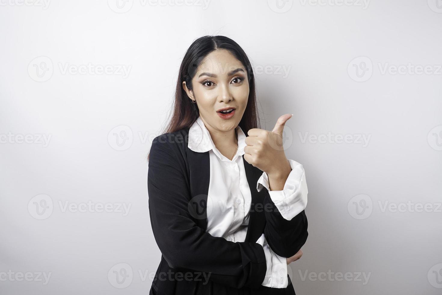 una mujer de negocios asiática emocionada con traje negro da un gesto de aprobación con la mano hacia arriba, aislada de fondo blanco foto