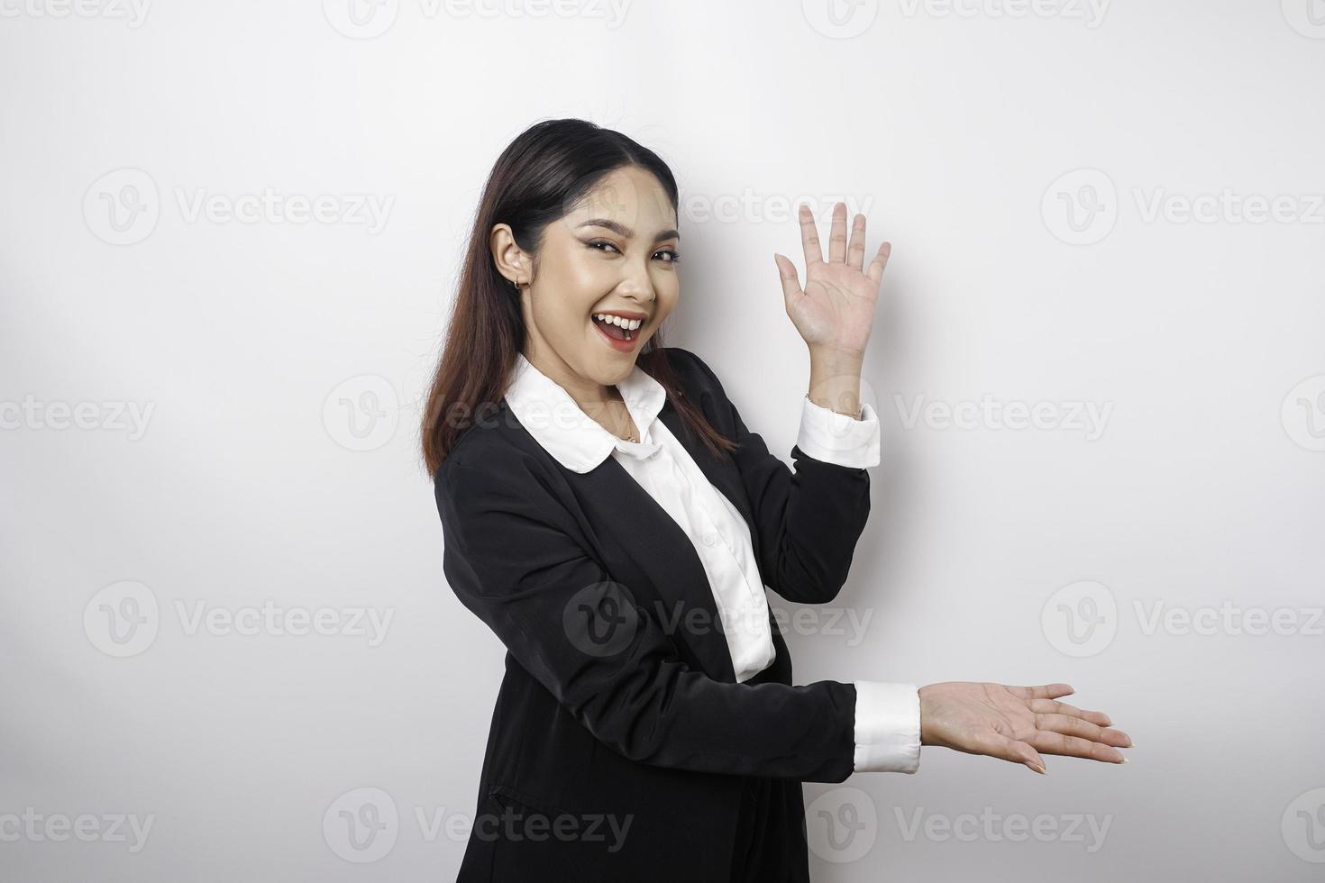 emocionada mujer de negocios asiática con traje negro apuntando al espacio de copia a su lado, aislada por fondo blanco foto