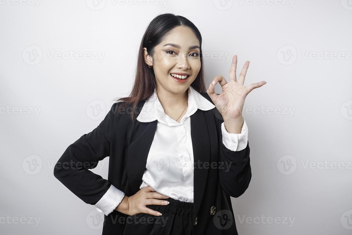 mujer de negocios asiática emocionada con un traje negro dando un gesto de mano bien aislado por un fondo blanco foto