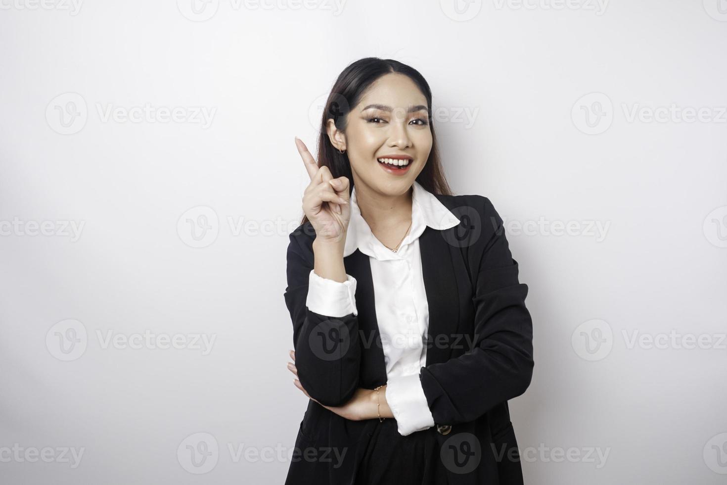 emocionada mujer de negocios asiática con traje negro apuntando al espacio de copia encima de ella, aislada de fondo blanco foto