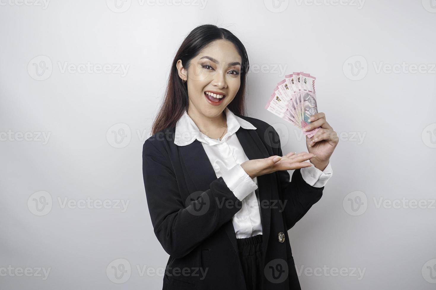 A happy young businesswoman is wearing black suit and holding cash money in Indonesian rupiah isolated by white background photo