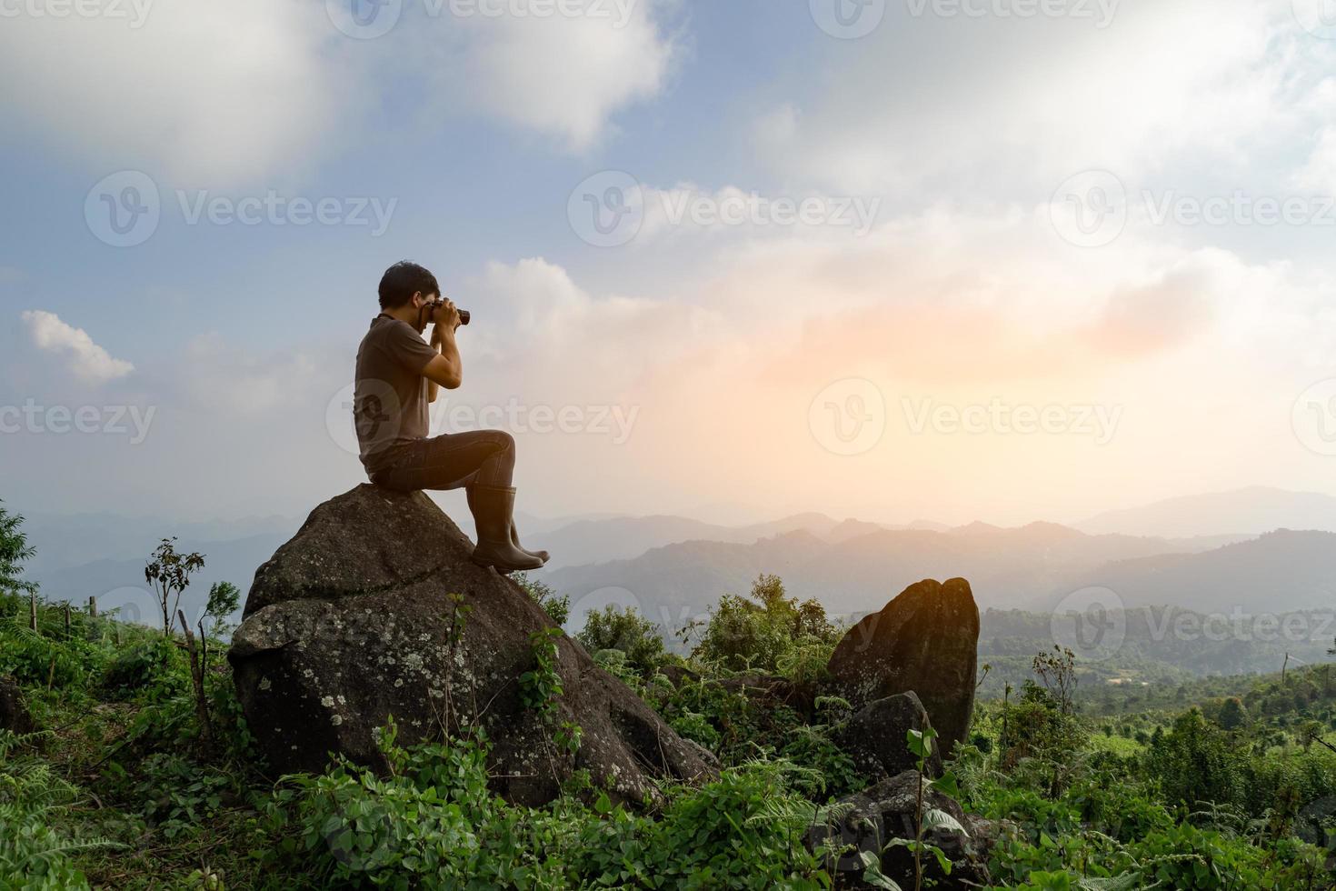 Wide angle shot of Asian man sitting on the rock and take photo, relax adventure nature adventure and explore concept computer sunrise light, copy space for individual text photo