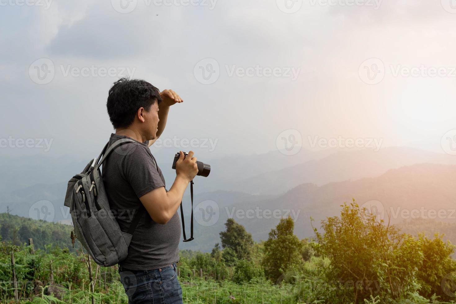 A sian man with his backpack and camera is travel alone and look at far a way, nature travel and environment concept, copy space for individual text photo