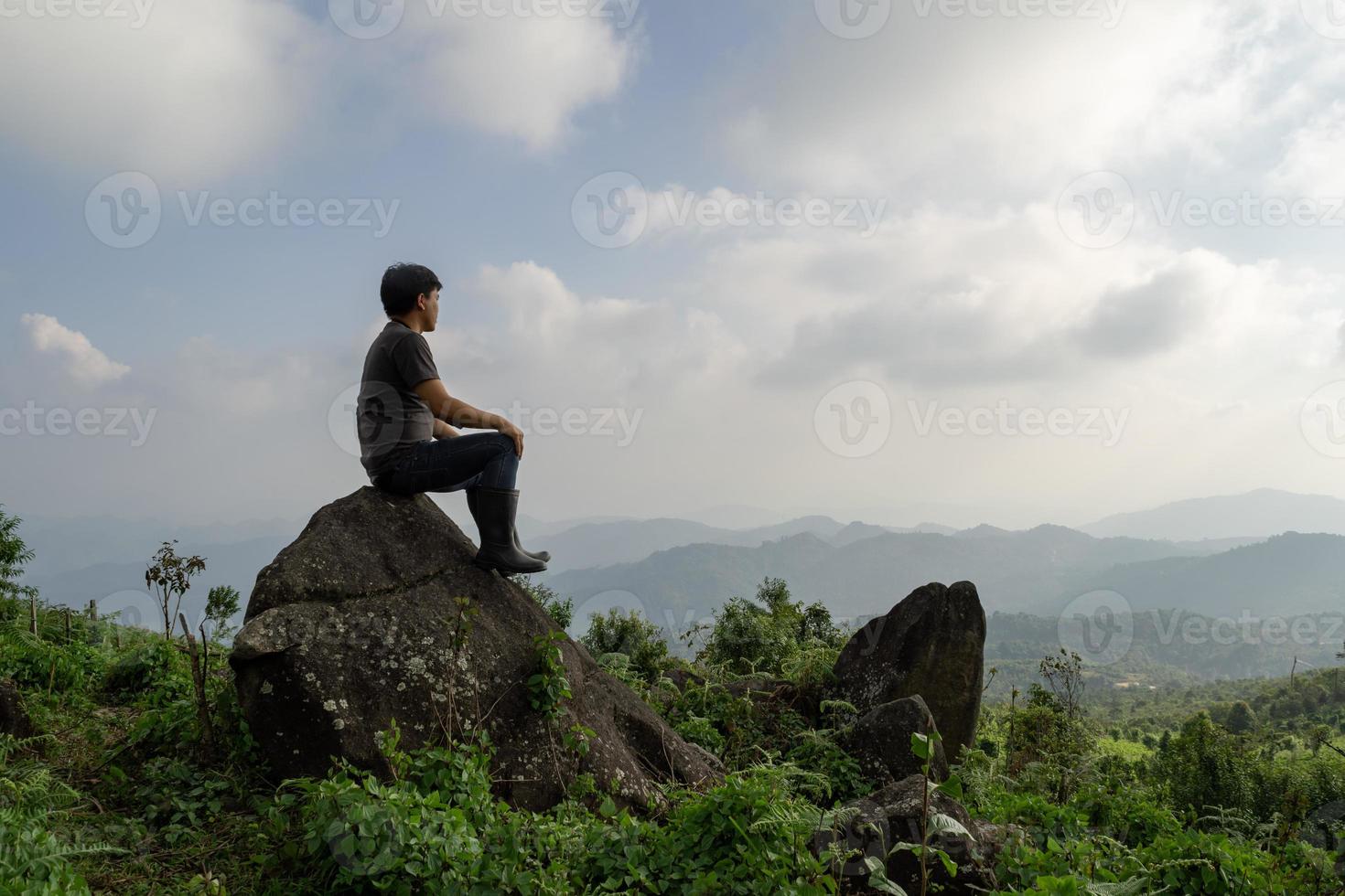 toma en gran angular de un hombre asiático sentado en la roca y mira una aventura lejana solo, viajes por la naturaleza y concepto de medio ambiente computadora luz del amanecer, espacio de copia para texto individual foto