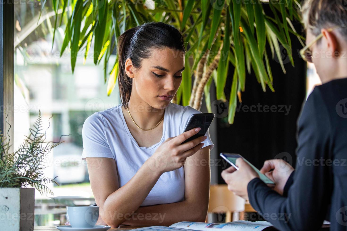 Mobile addiction concept, friends ignoring each other using smartphones relaxing in coffee shop, Obsessed with new apps or social networks, phone addicts lost in news online photo