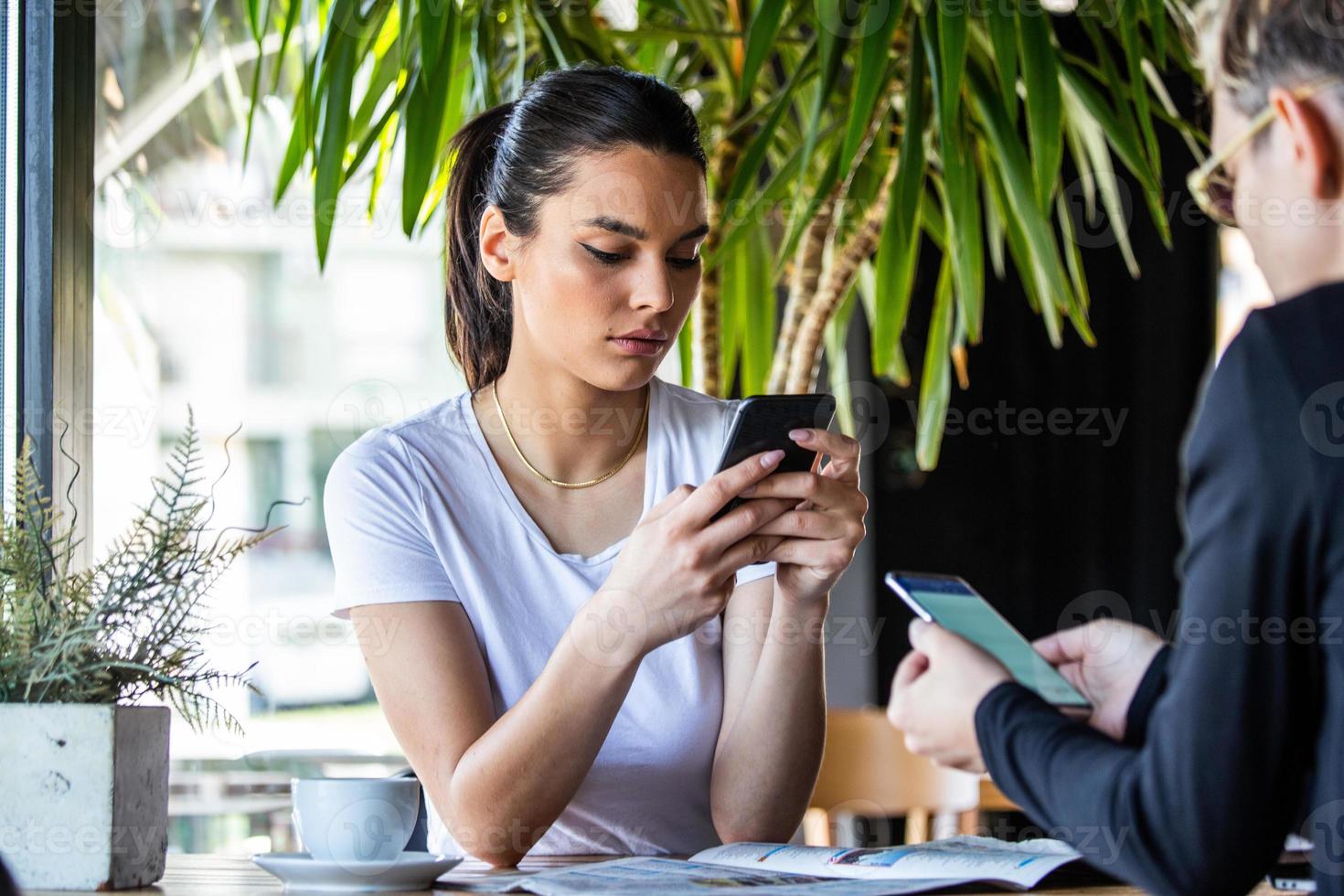 Mobile addiction concept, friends ignoring each other using smartphones relaxing in coffee shop, Obsessed with new apps or social networks, phone addicts lost in news online photo