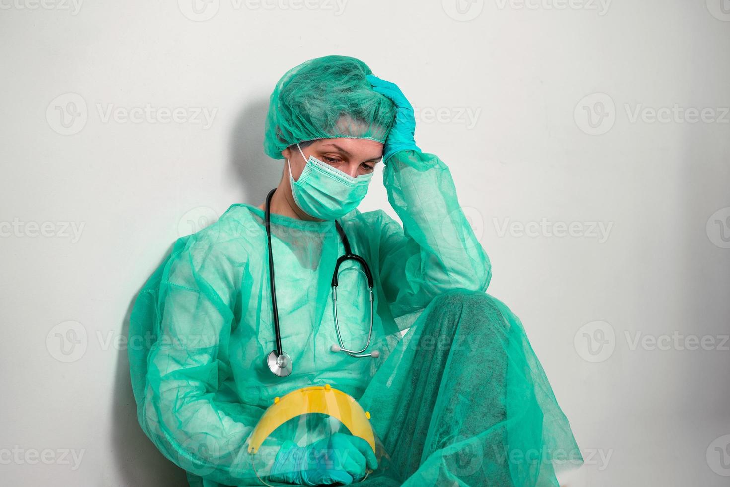 Coronavirus concept. COVID-19. Young female doctor in protective suit uniform, face mask and rubber gloves, before patient examination feeling exhausted and worried. Doctors are heroes. photo