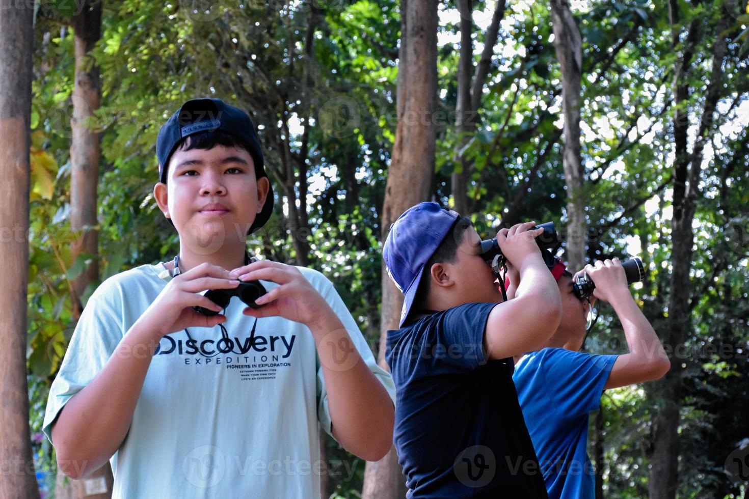 retrato de niños asiáticos usando binoculares para observar aves en el bosque tropical con sus amigos, idea para aprender criaturas y animales salvajes fuera del aula, enfoque suave. foto