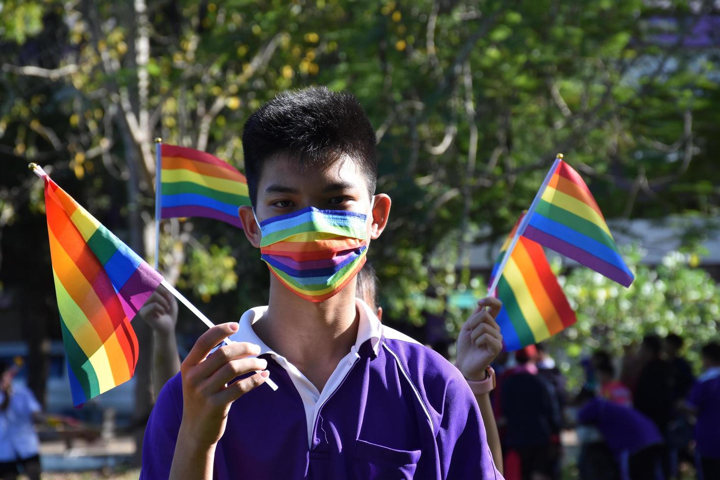 retrato joven asiático sostiene la bandera del arco iris, símbolo lgbt, en las manos mientras se une a su actividad lgbt en la escuela, concepto para la celebración de la comunidad lgbt en el mes del orgullo, junio de 2023, en todo el mundo. foto