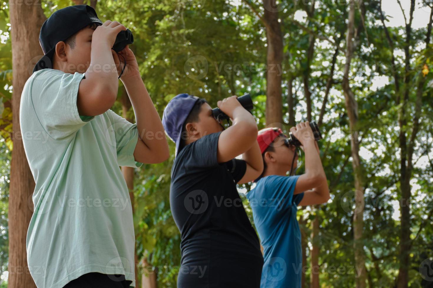 retrato de niños asiáticos usando binoculares para observar aves en el bosque tropical con sus amigos, idea para aprender criaturas y animales salvajes fuera del aula, enfoque suave. foto