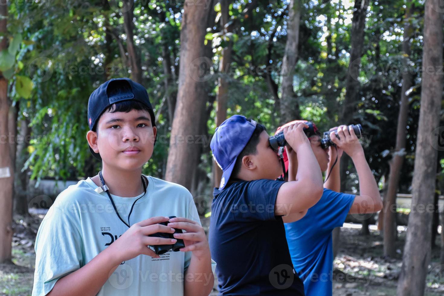 Portrait Asian boys using binoculars to watch birds in tropical forest with his friends, idea for learning creatures and wildlife animals outside the classroom, soft focus. photo