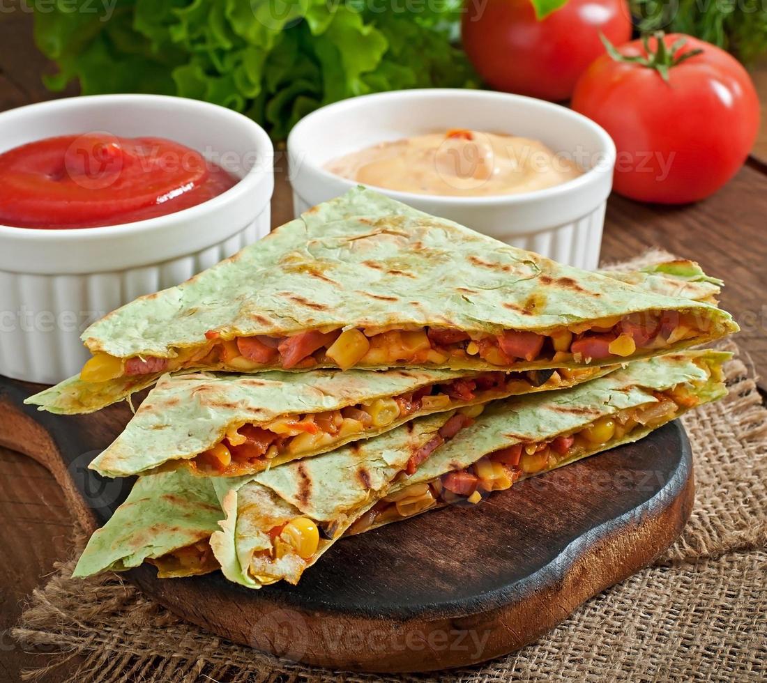 Quesadilla mexicana en rodajas con verduras y salsas sobre la mesa foto