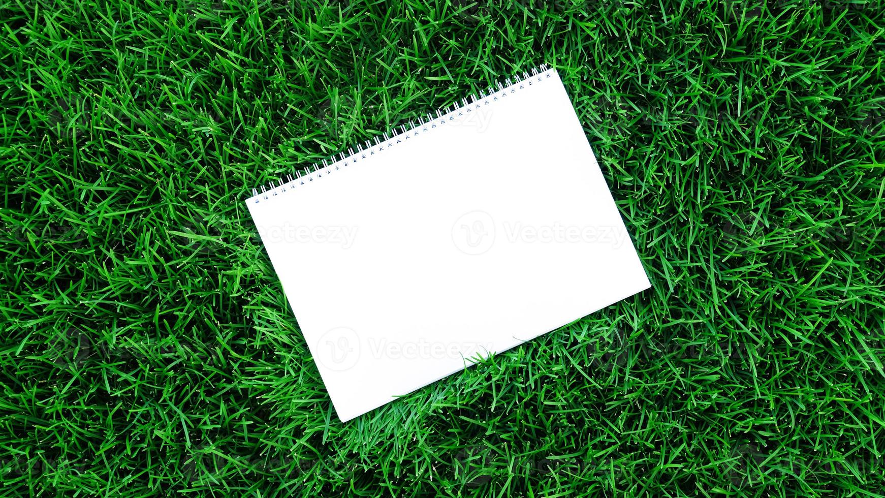 Empty white paper on green grass background. For message flat lay with copy space for text or products presentation. Nature concept, business and lifestyle environment. photo